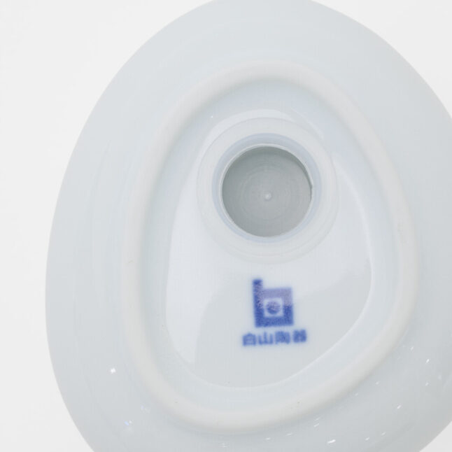 The underside of a white Hakusan Porcelain salt shaker with the blue logo next to the hole to refill the salt