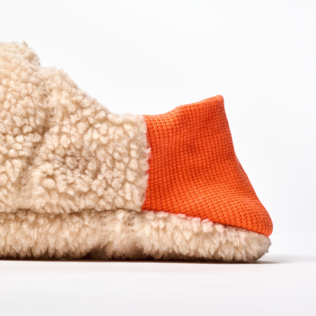 A reversible slipper with a beige shaggy fabric with a orange ribbed heel from Japan House London.