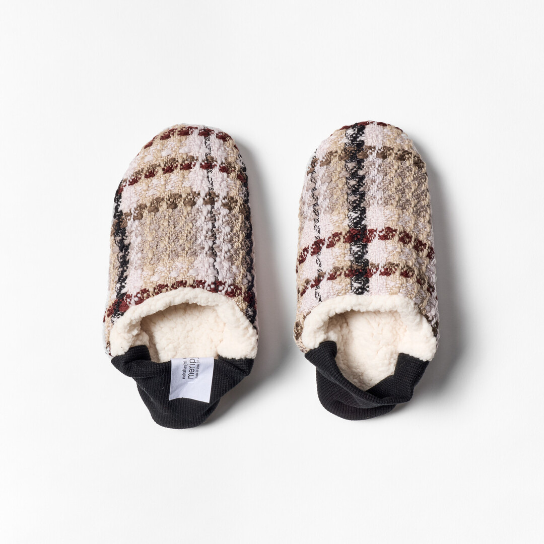 A pair of reversible slippers with a beige and brown tartan fabric and white sheep boa fabric on the other side with a black ribbed heel from Japan House London.