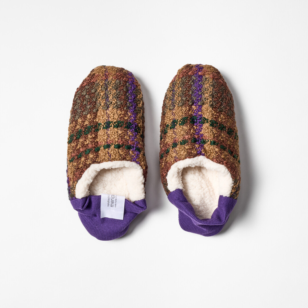 A pair of reversible slippers with a green and brown tartan fabric and white sheep boa fabric on the other side with a purple ribbed heel from Japan House London.