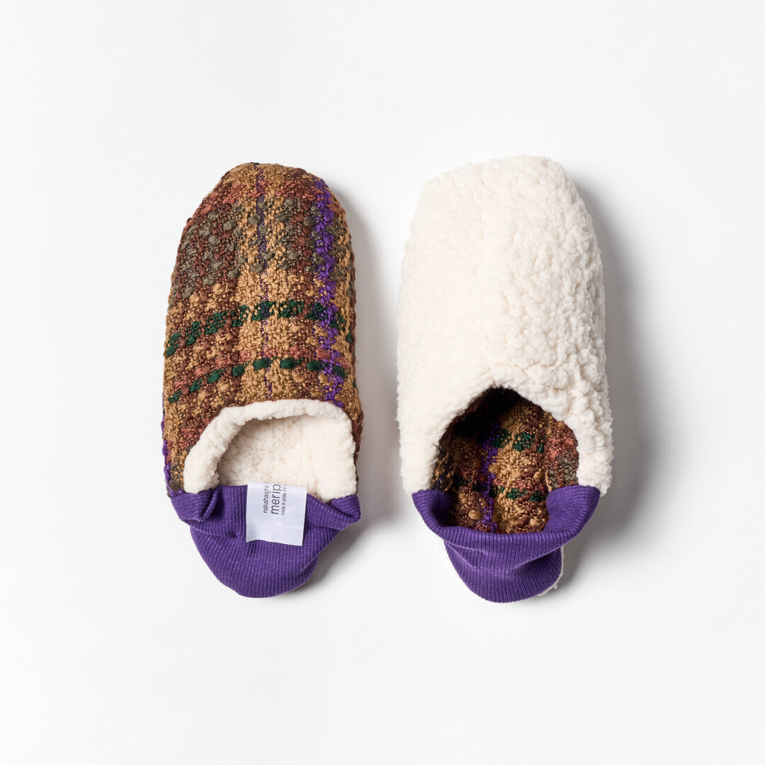A pair of reversible slippers with a green and brown tartan fabric and white sheep boa fabric on the other side with a purple ribbed heel from Japan House London.