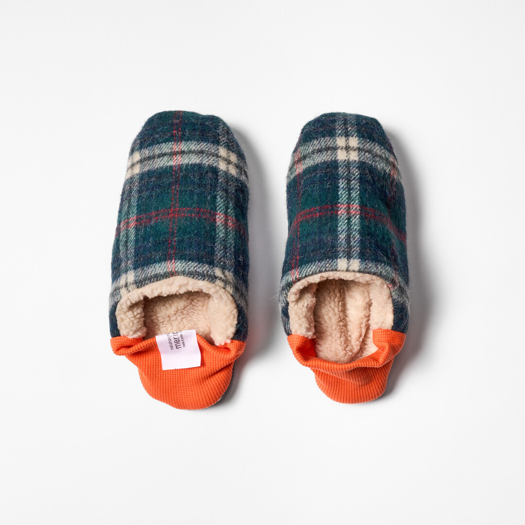 A pair of reversible slippers with a blue and green tartan fabric and beige shaggy fabric on the other side with a orange ribbed heel from Japan House London.