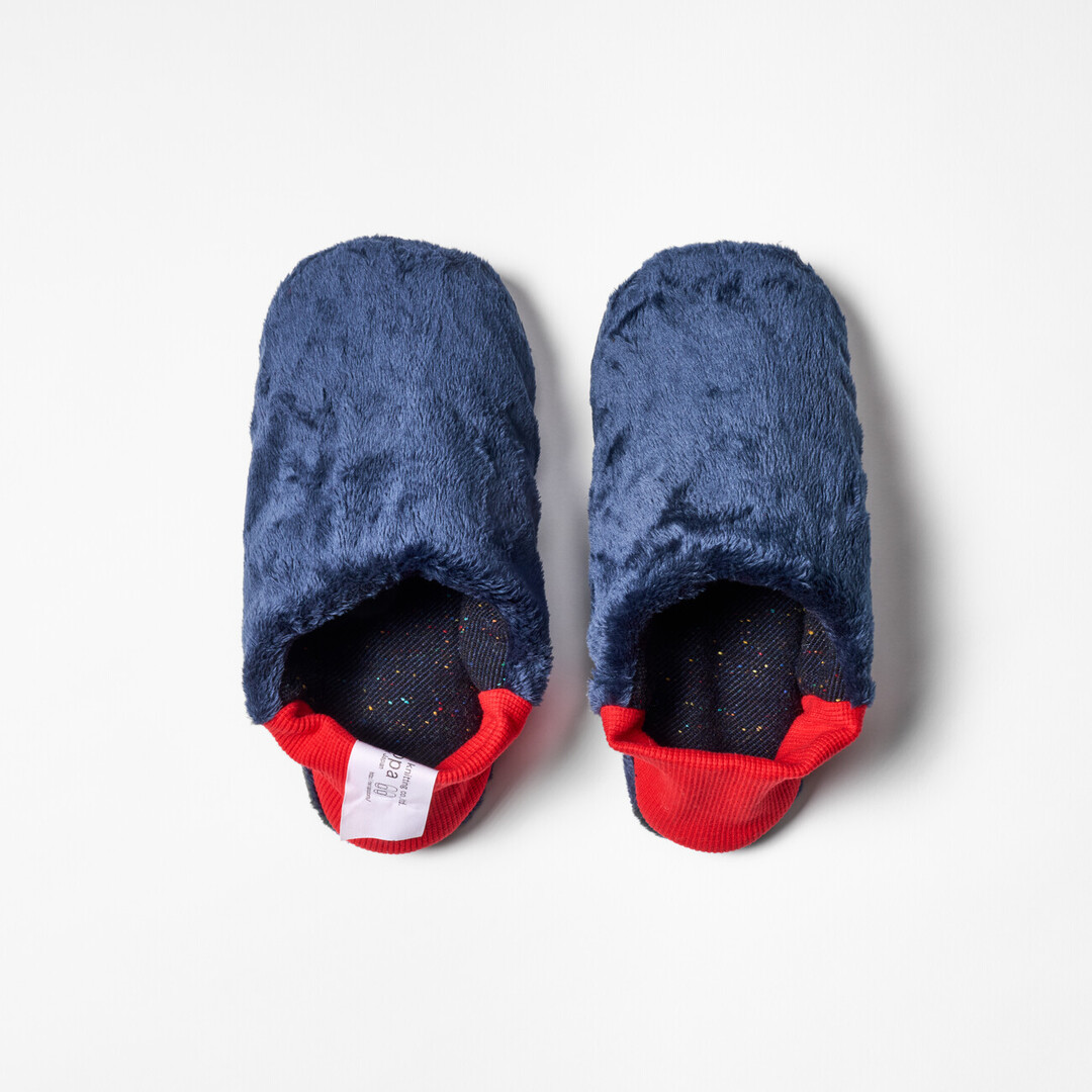 A pair of reversible slippers with a navy blue with speckle fabric and blue furry fabric on the other side with a red ribbed heel from Japan House London.