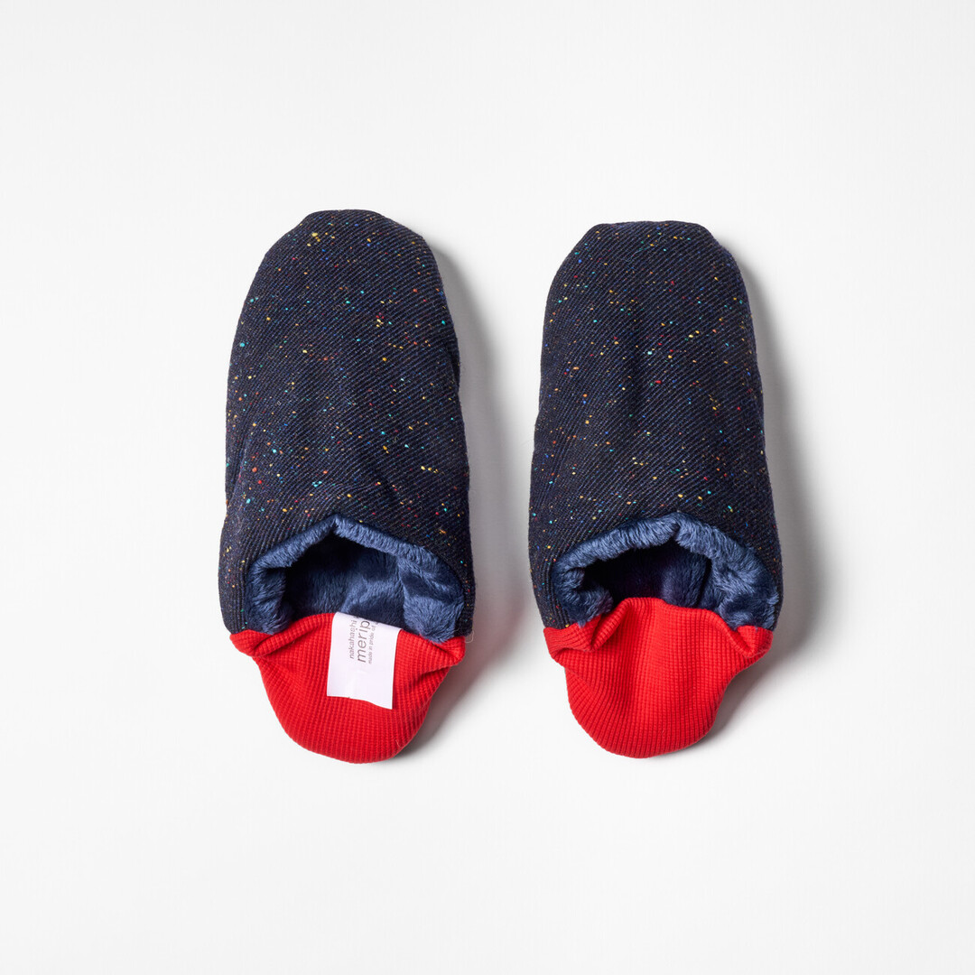 A pair of reversible slippers with a navy blue with speckle fabric and blue furry fabric on the other side with a red ribbed heel from Japan House London.