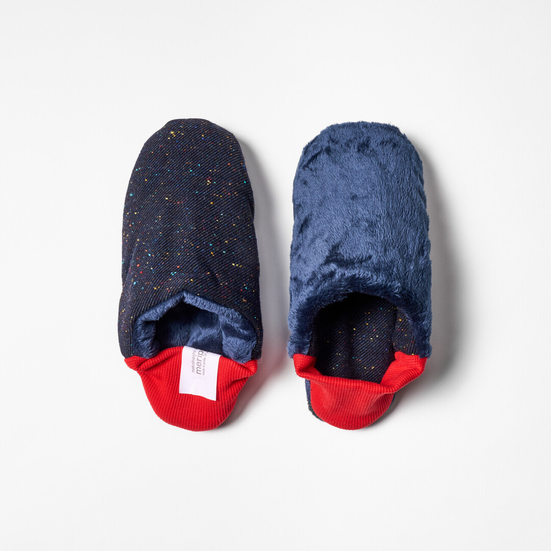 A pair of reversible slippers with a navy blue with speckle fabric and blue furry fabric on the other side with a red ribbed heel from Japan House London.