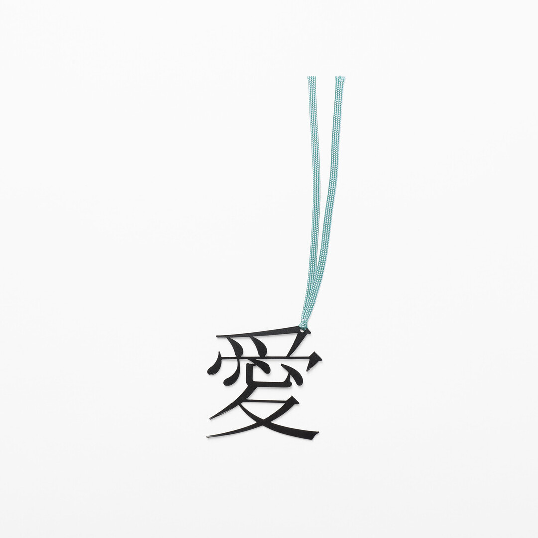A bookmark in the shape of the character of love in Japanese with a blue ribbon attached from Japan House London.