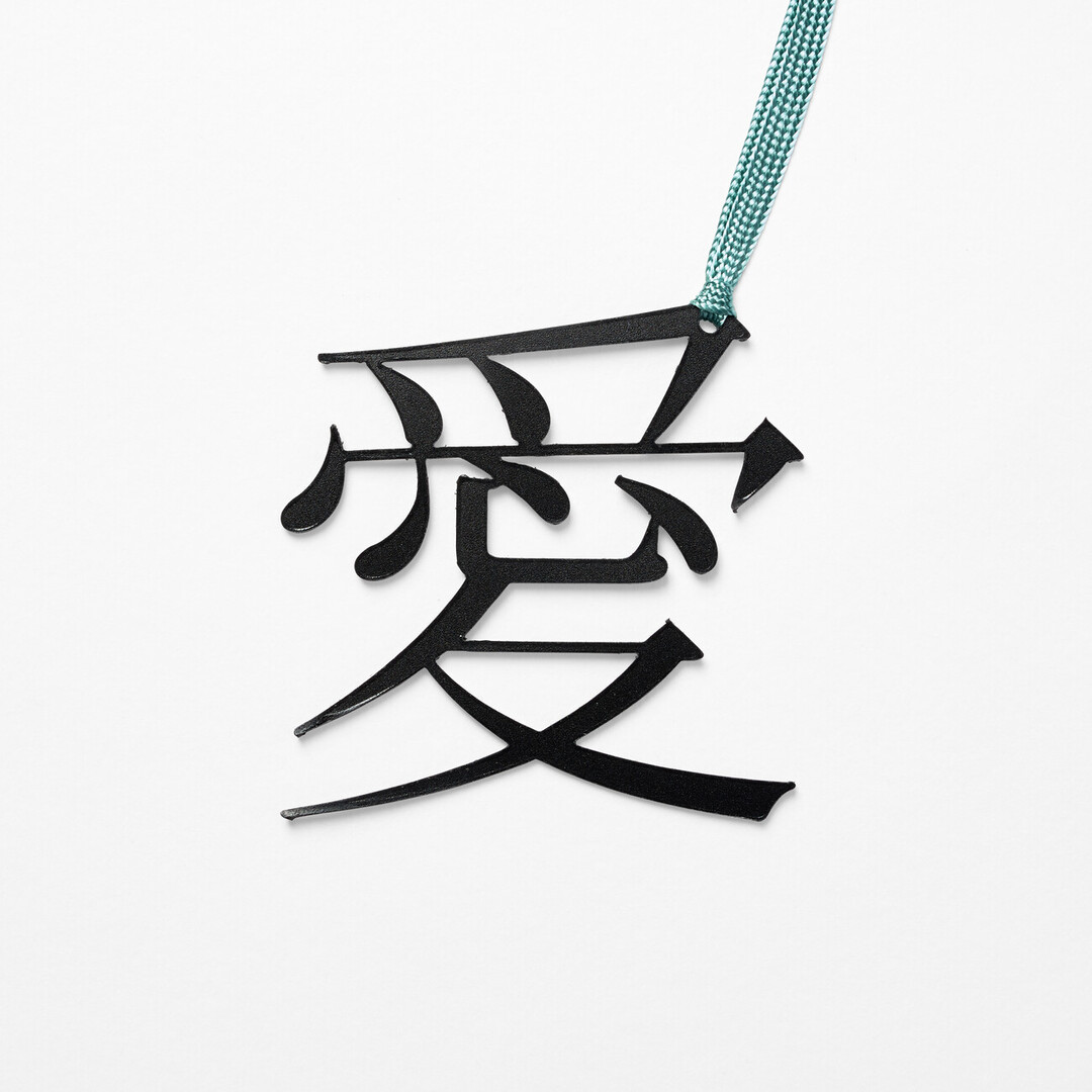A bookmark in the shape of the character of love in Japanese with a blue ribbon attached from Japan House London.