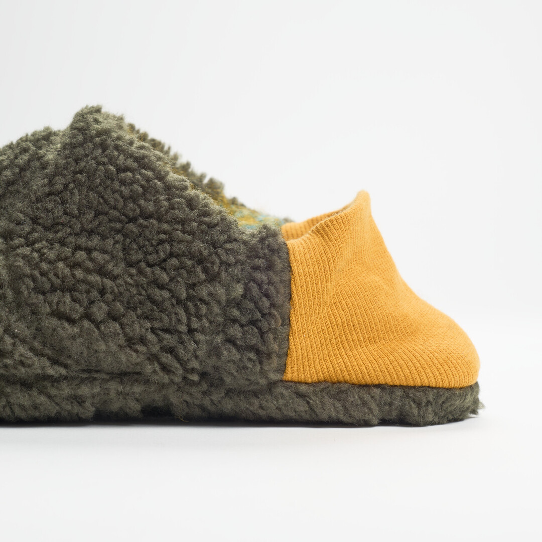 A reversible slipper with a felted green and blue blended fabric and a dark green shaggy fabric on the other side with a yellow ribbed heel from Japan House London.