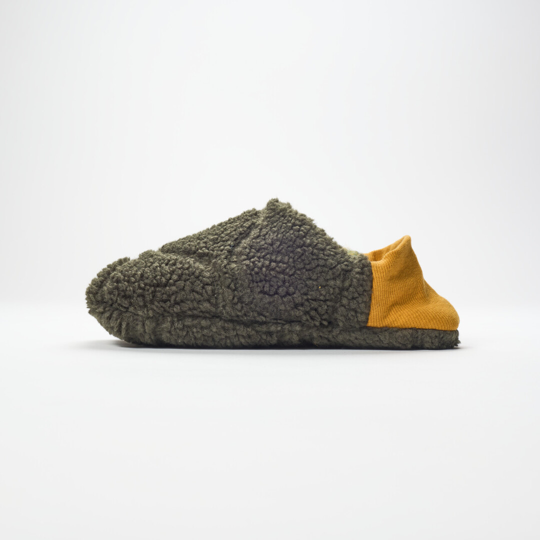 A reversible slipper with a felted green and blue blended fabric and a dark green shaggy fabric on the other side with a yellow ribbed heel from Japan House London.