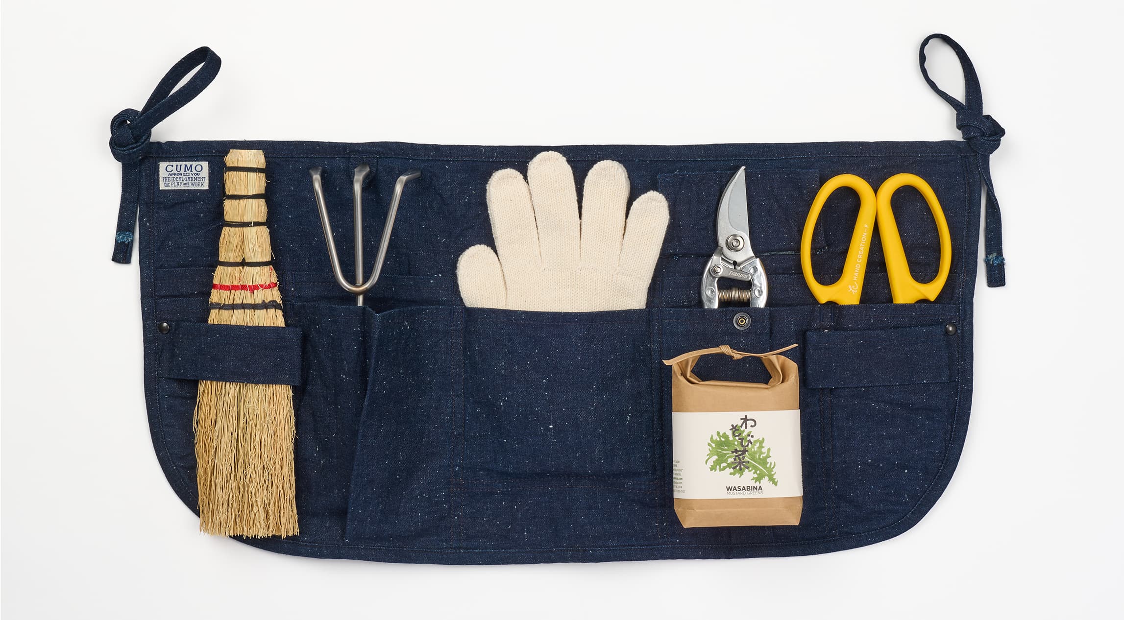 An indigo short apron with gardening tools in the pockets and belts from Japan House London.