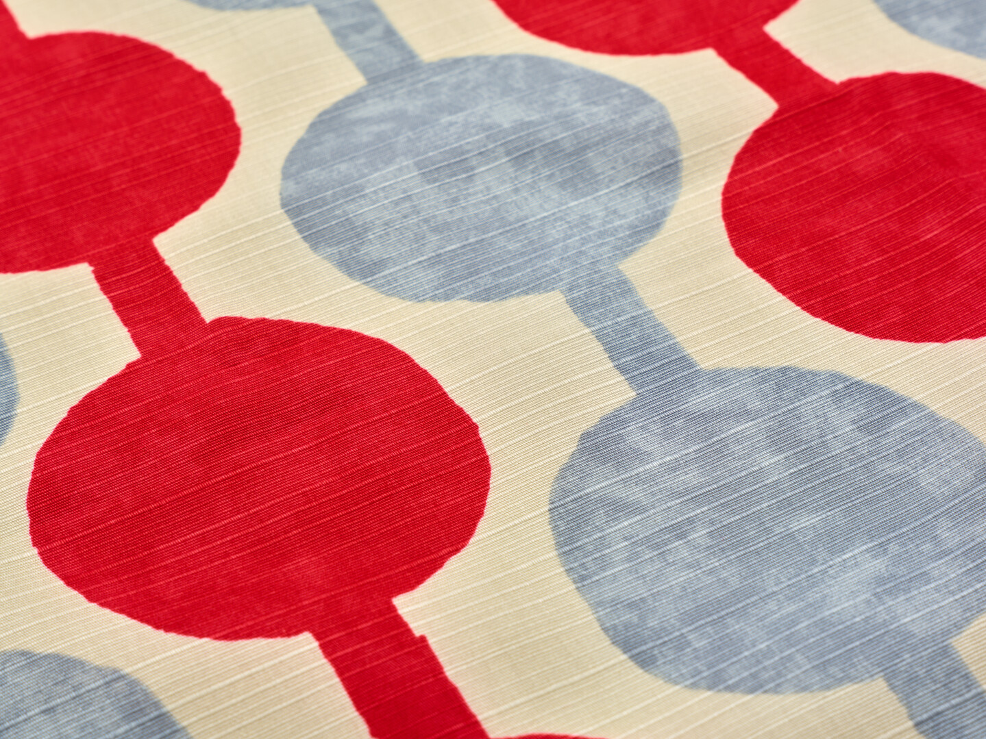 A furoshiki with red and grey pattern of spots and stripes on a cream background from Japan House London.