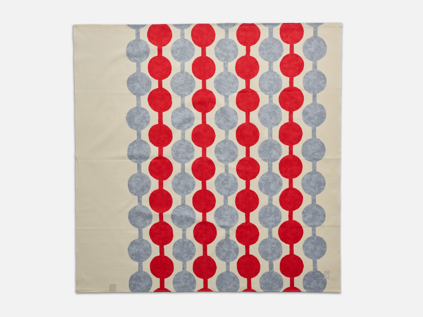 A furoshiki with red and grey pattern of spots and stripes on a cream background from Japan House London.