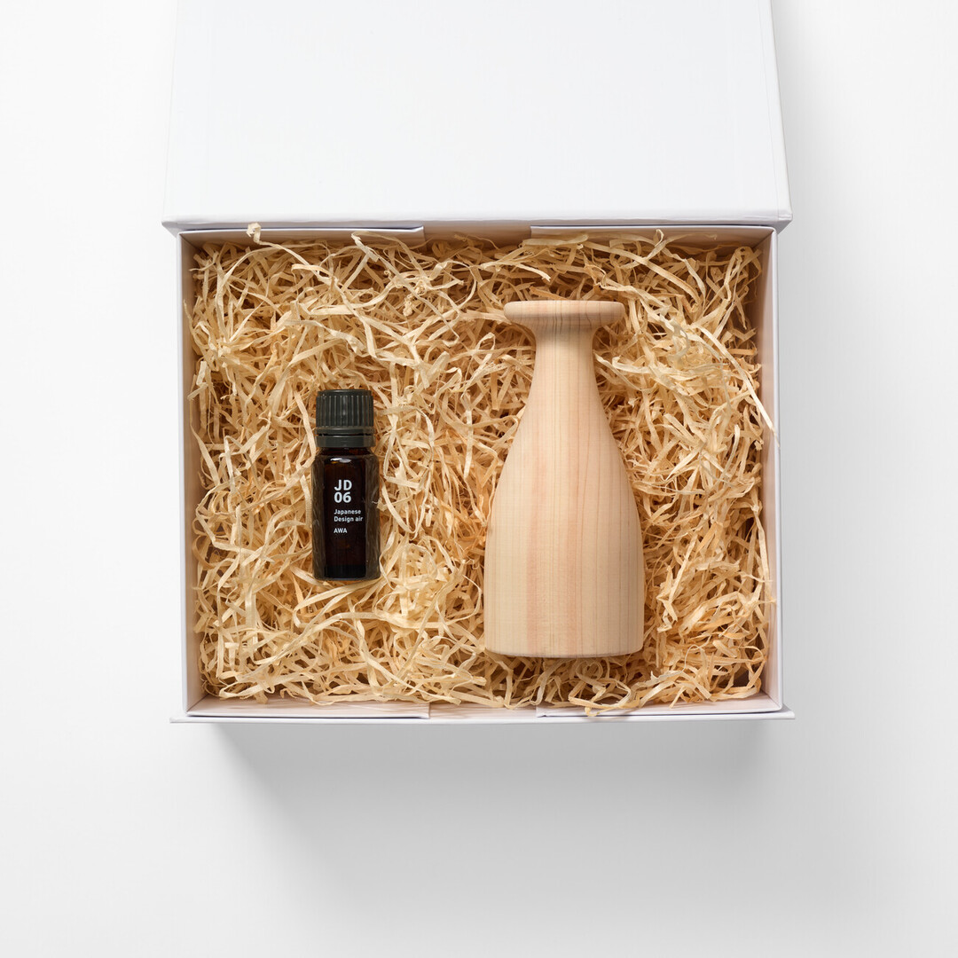 A white box filled with thin strips of wooden filler and a wooden aroma diffuser and a bottle of aroma oil as the Japanese aroma gift box from Japan House London.