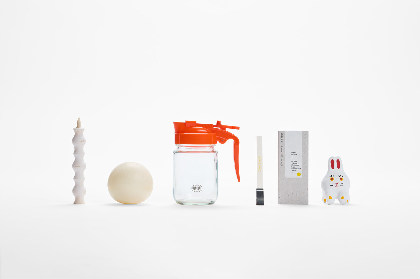 A row of stocking fillers of a Takizawa Candle, soap ball, Okawa Glass syrup dispenser, washi incense and rabbit hariko from Japan House London.