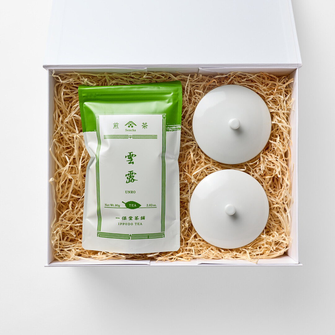 A white gift box with a bag of Unro green tea with two white tea cups with lids in wood shavings from Japan House London.