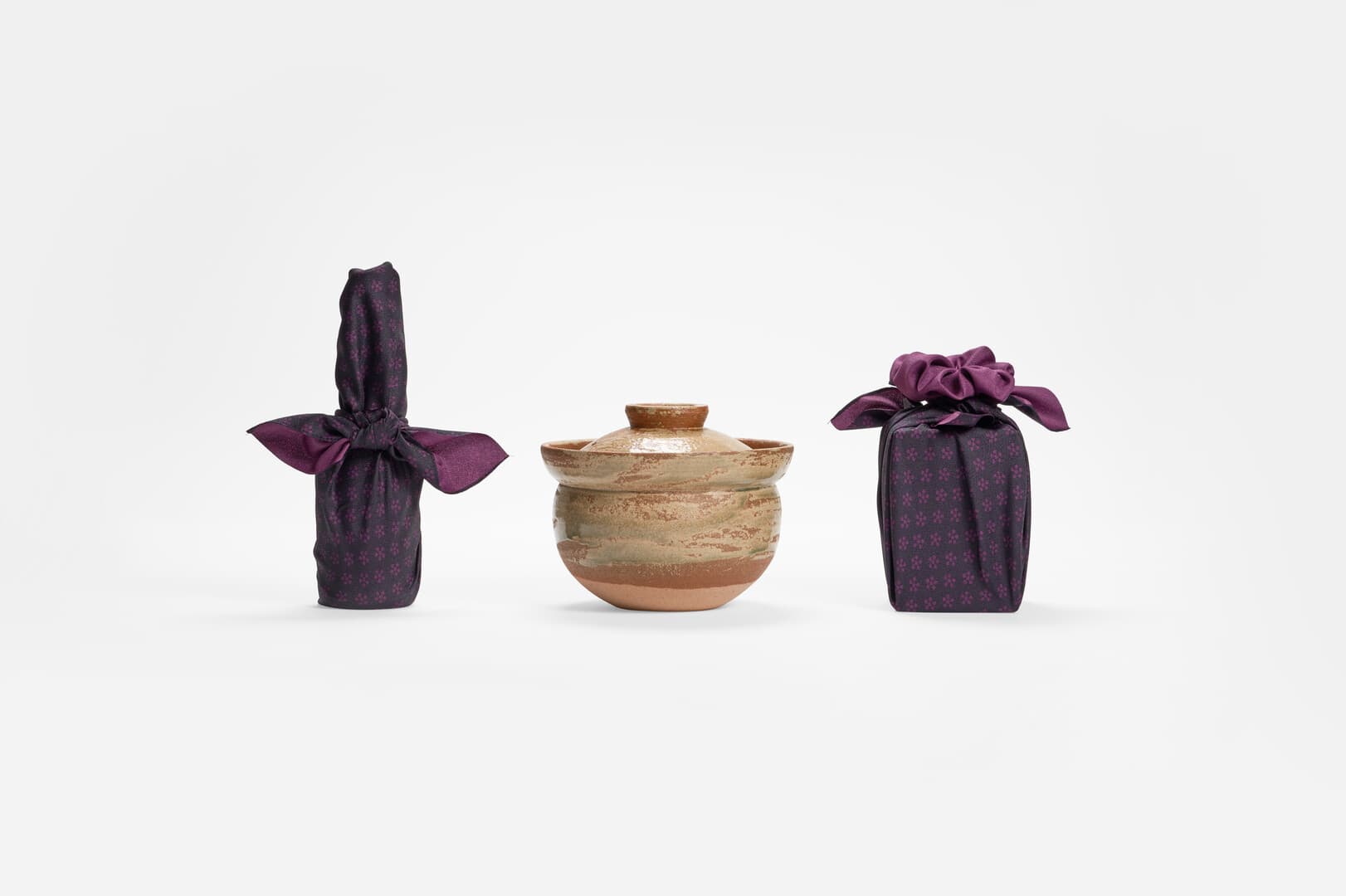Two presents wrapped in purple furoshiki on the either side of a earthenware pot in the middle from Japan House London.