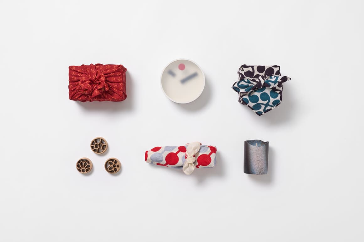 Two rows of presents, three wrapped in furoshiki, the other three are three brass flower frogs, a Kehai clock and a Shigaraki-yaki candle from Japan House London.