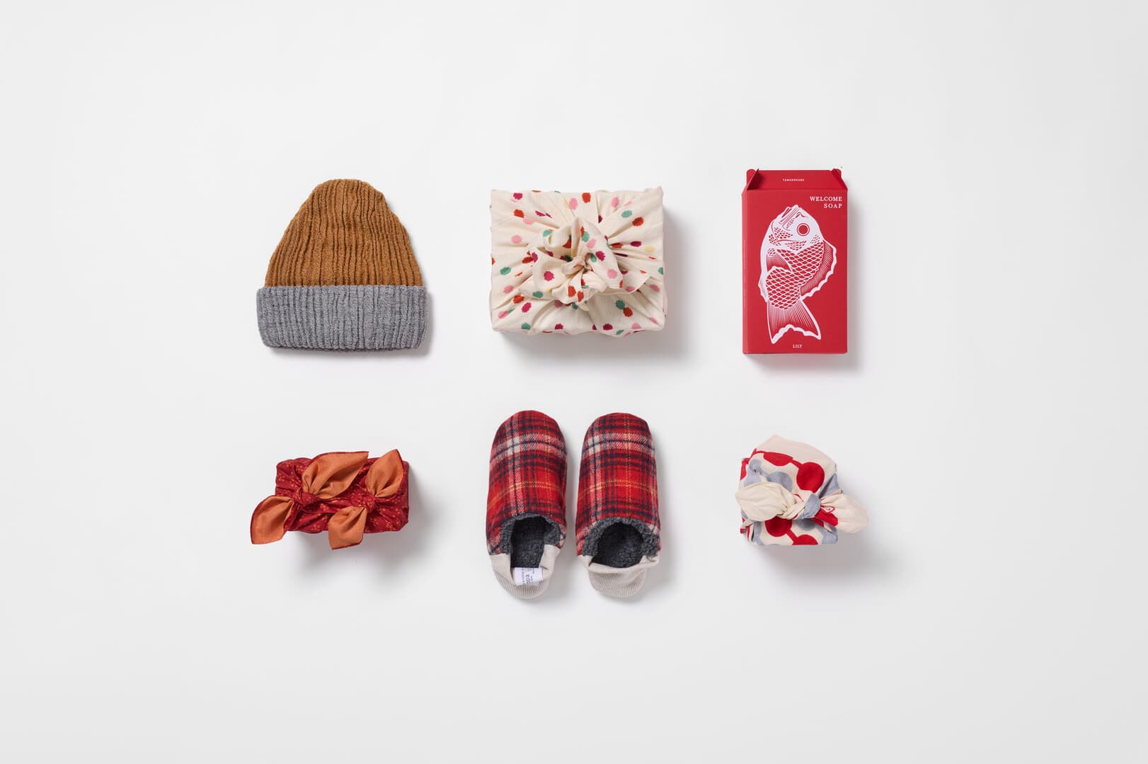 Two rows of presents, three wrapped in furoshiki, the other three are 8 way cap, sea bream soap and merippa Japanese slippers from Japan House London.