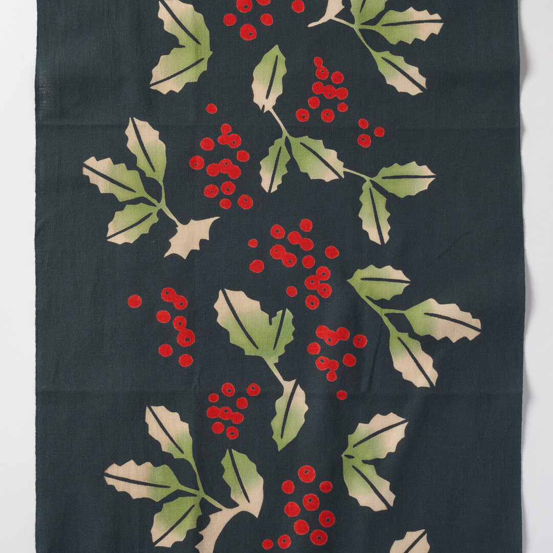 A dark green tenugui with a holly pattern running through the centre from Japan House London.