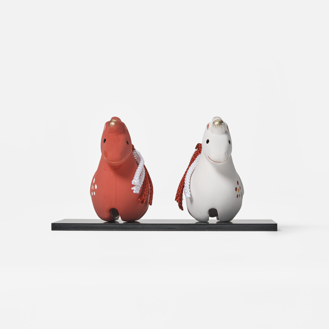A pair of earthenware bell in red and white in the shape of a horse on a platform by Kyugetsu from Japan House London.