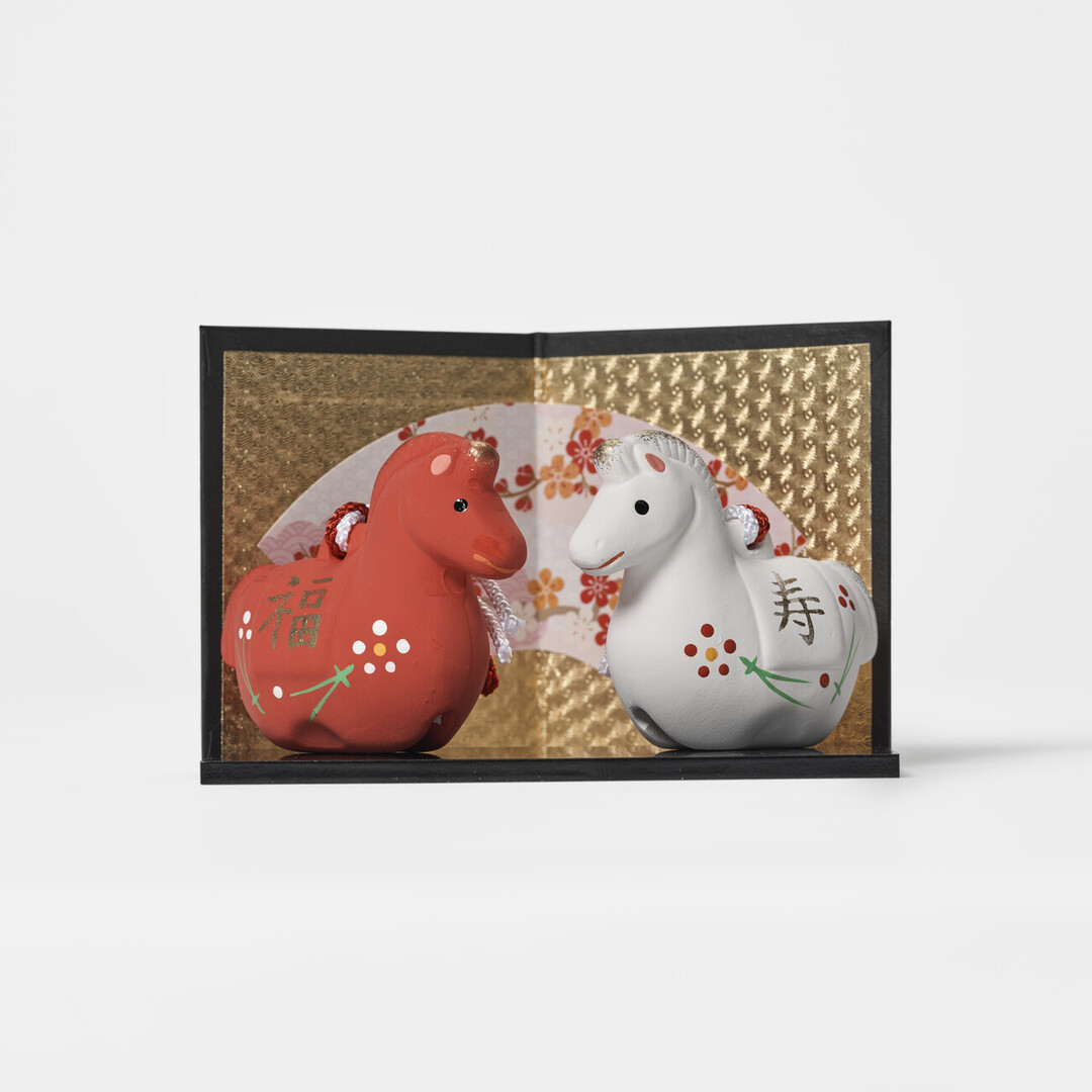 A pair of earthenware bell in red and white in the shape of a horse on a platform and gold screen by Kyugetsu from Japan House London.