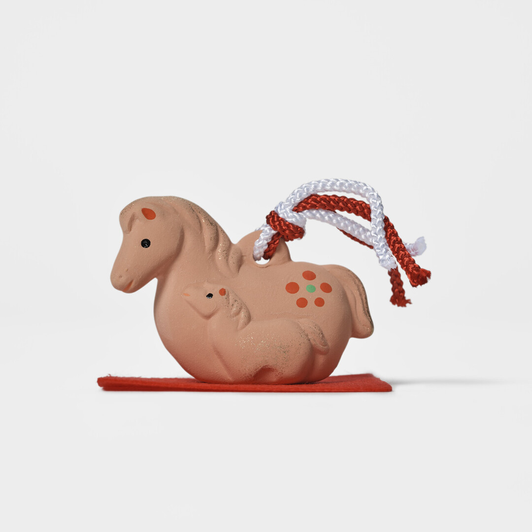 An earthenware bell in the shape of a mare and foal on a red mat by Kyugetsu from Japan House London.