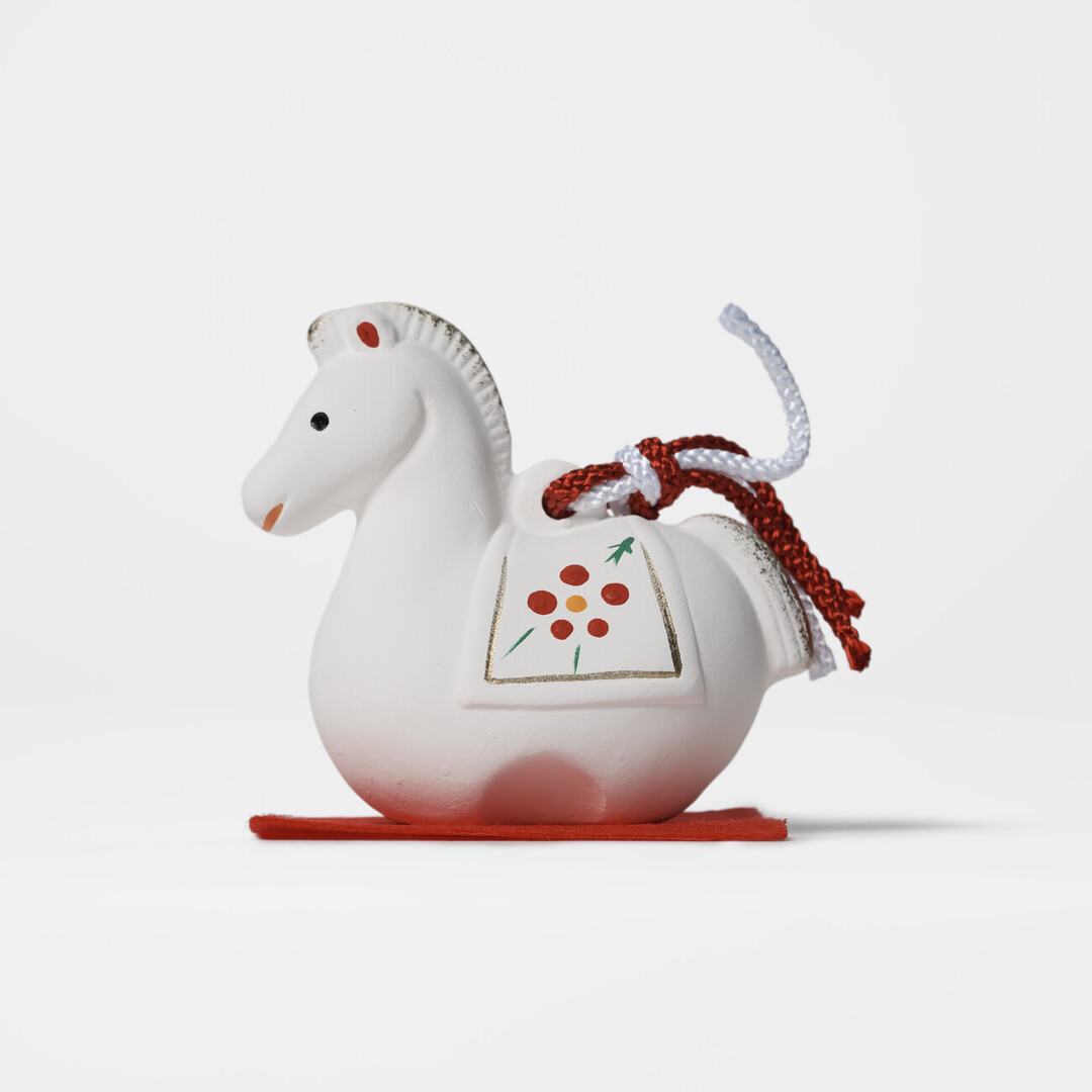 An earthenware bell in the shape of a white horse on a red mat by Kyugetsu from Japan House London.