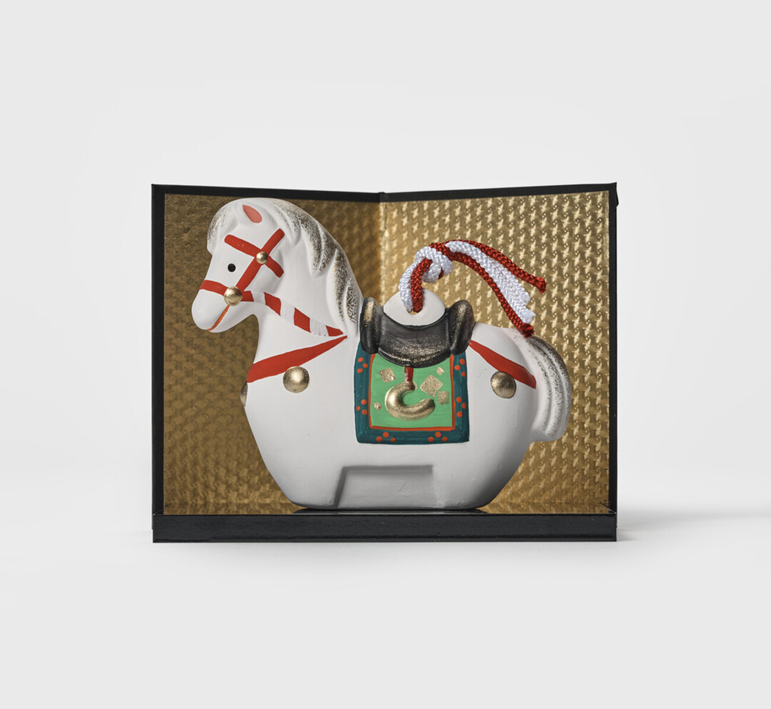 An earthenware horse bell on a black platform and gold screen by Kyugetsu from Japan House London.