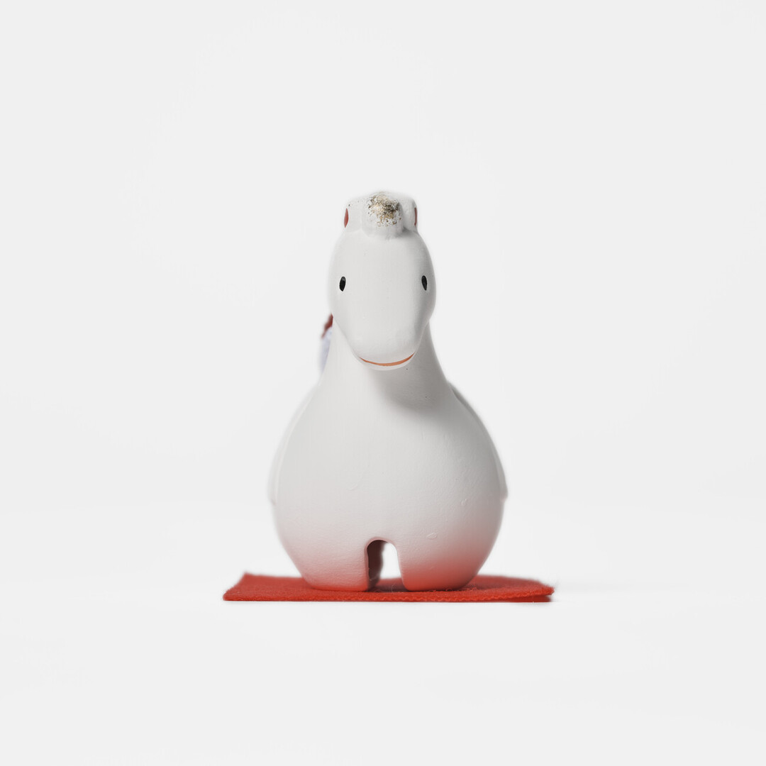An earthenware bell in the shape of a white horse on a red mat by Kyugetsu from Japan House London.