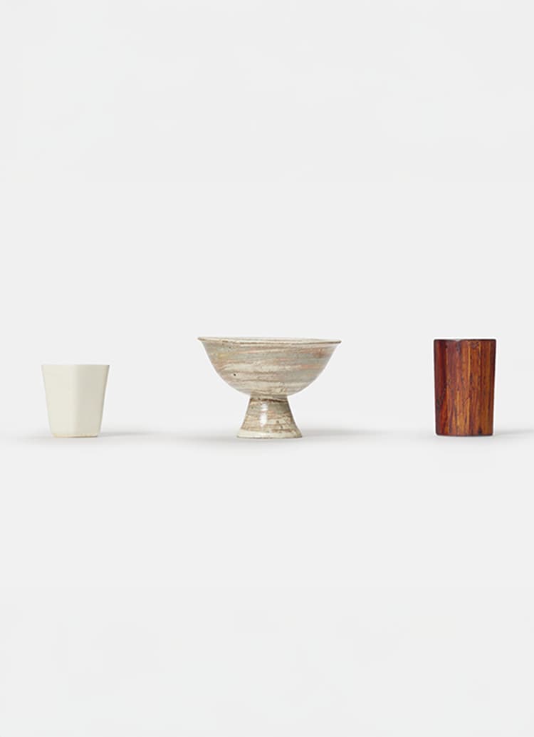 Three small vessels in a row, two ceramic and one wooden from Hyakko 100 Makers exhibition at Japan House London.