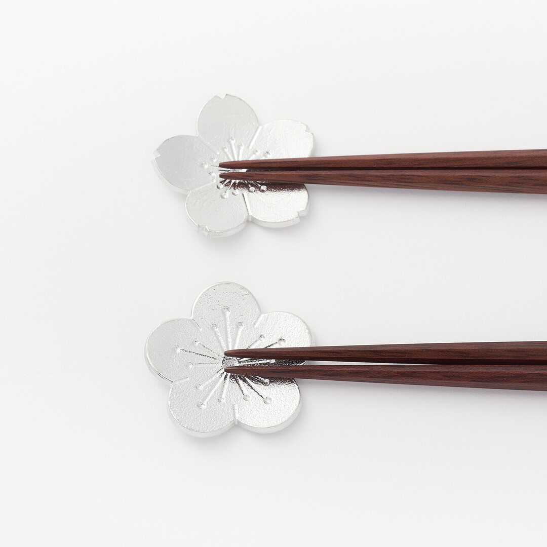 A sakura and plum flower shaped tin chopstick rests with chopsticks resting on each by Nousaku from Japan House London.