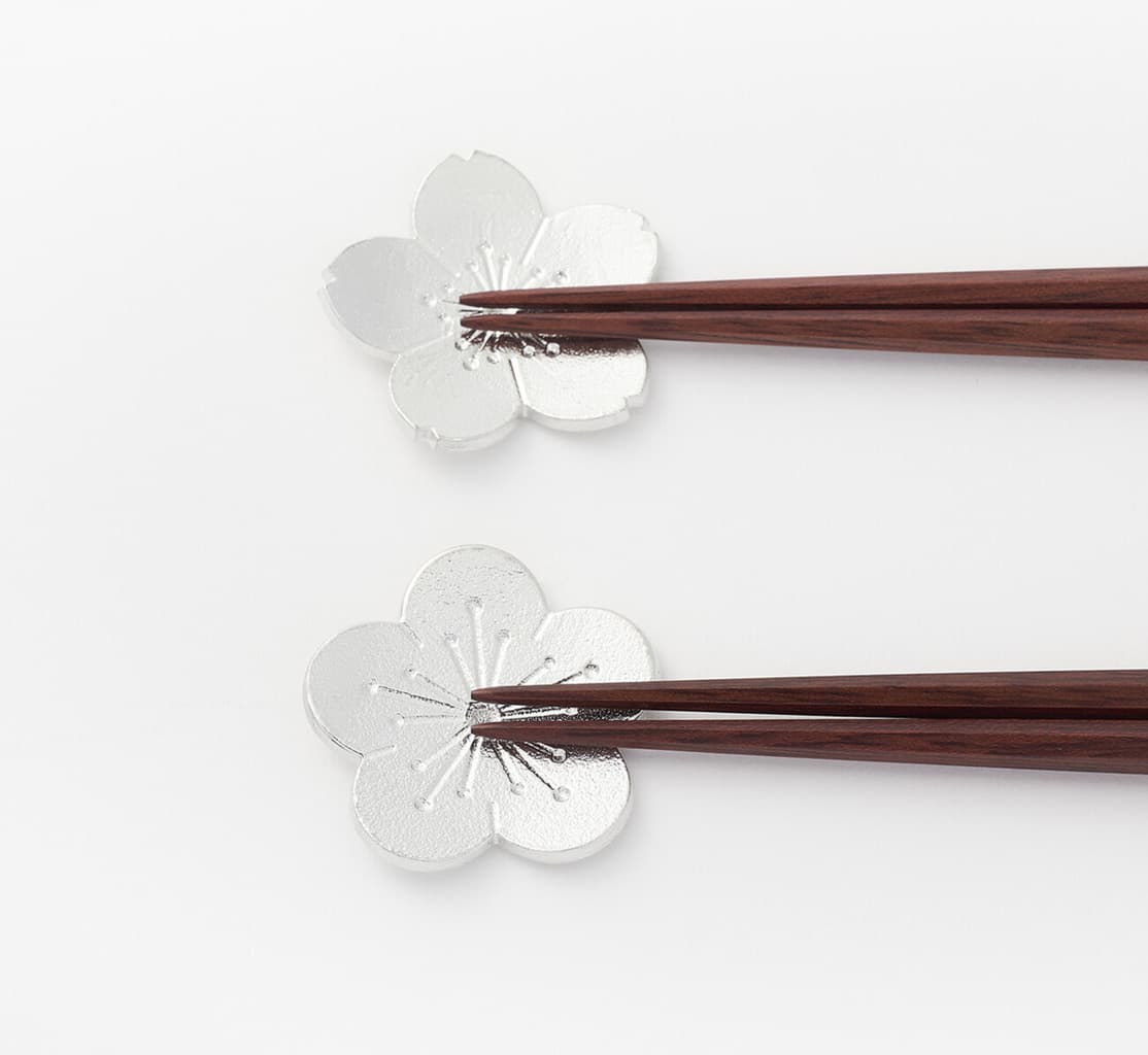 Two silver tin chopstick holders shaped as sakura and plum flower with chopsticks on each from Japan House London.