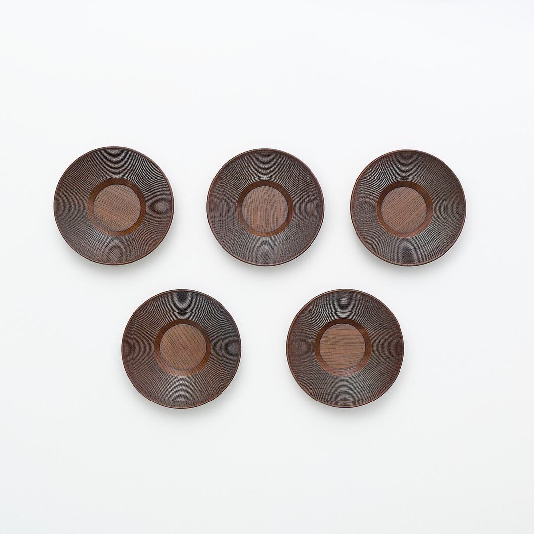 Five dark brown wooden saucers with carved ring details on the rim by Gato Mikio from Japan House London.