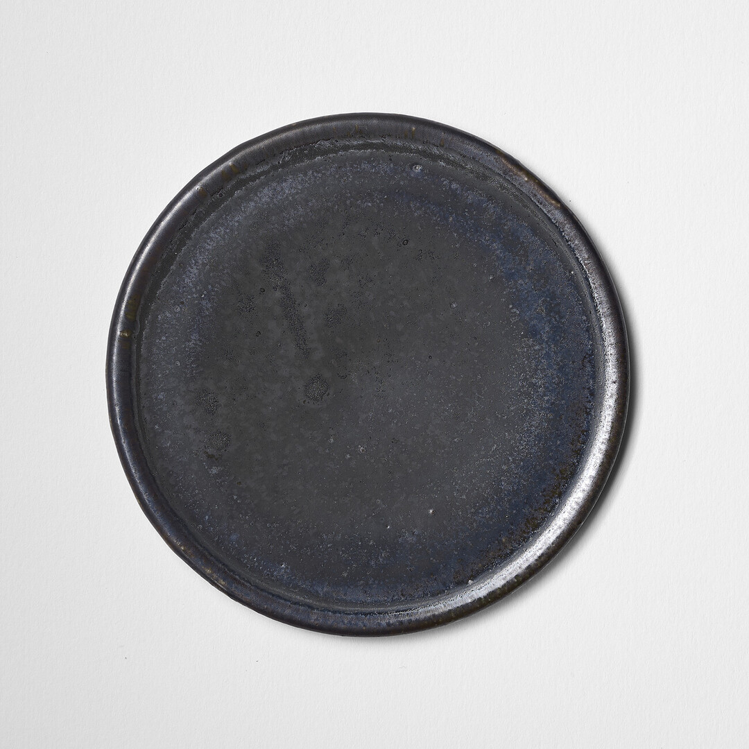 A small circular ceramic plate with black glaze by Shimomura Atsushi from Japan House London.