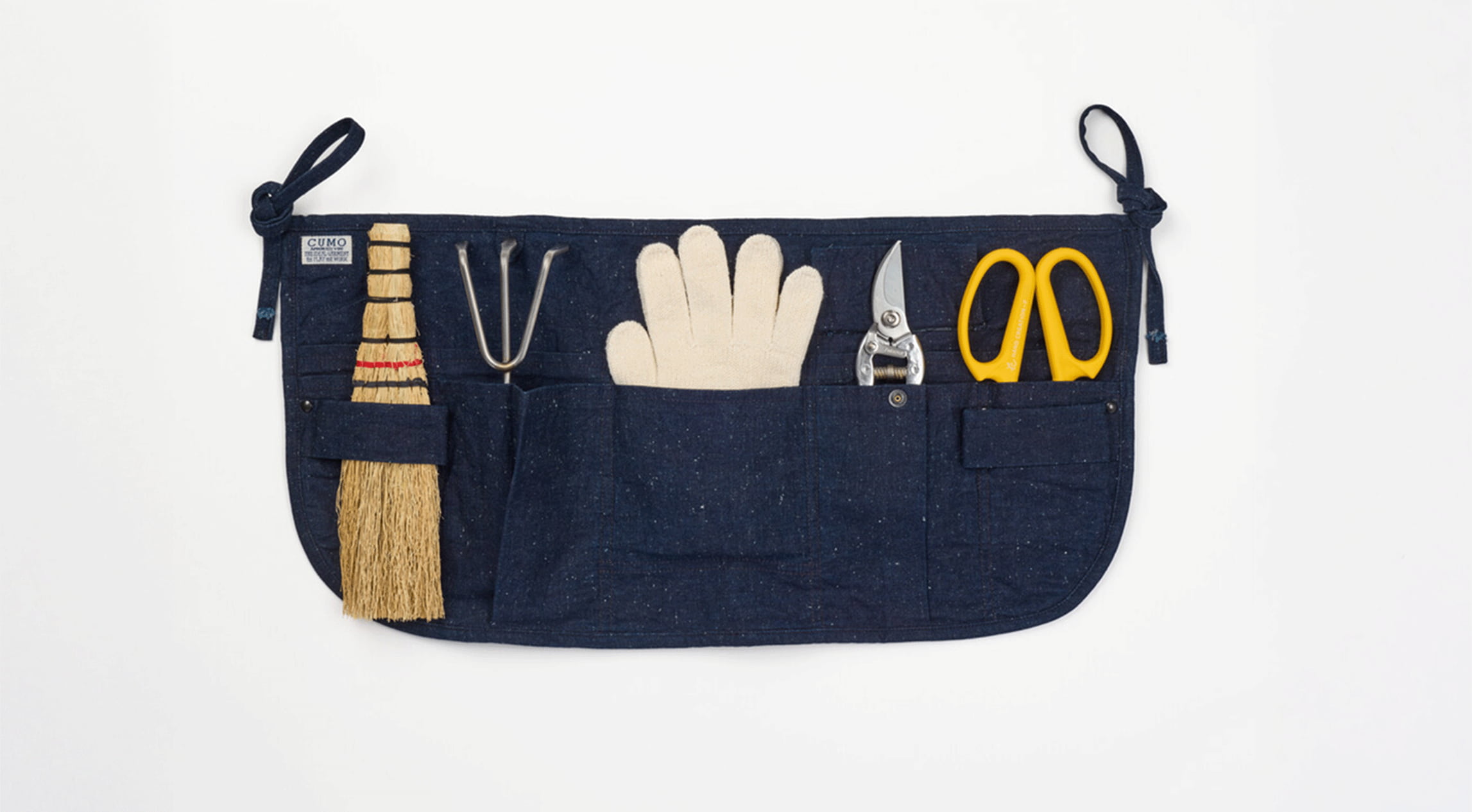 An indigo apron with gardening tools in pockets from Japan House London.