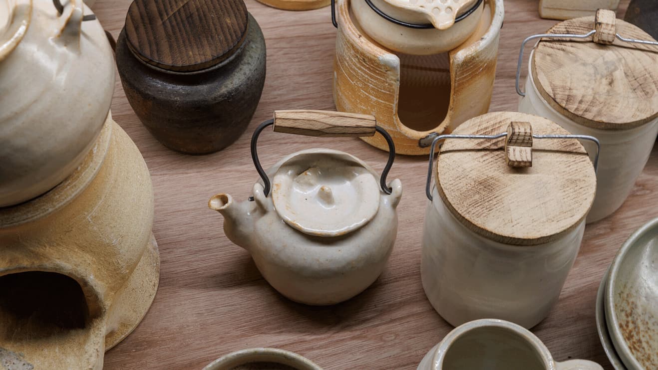Several ceramic pots and tea pots on a wooden surface at Japan House London.