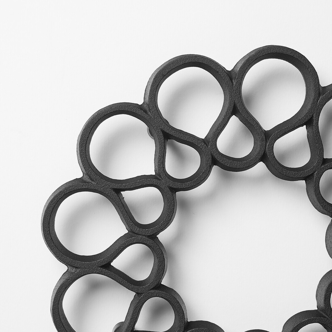 A black iron trivet shaped with undulating lines in a donut form by OIGEN Foundry Co., Ltd. from Japan House London.