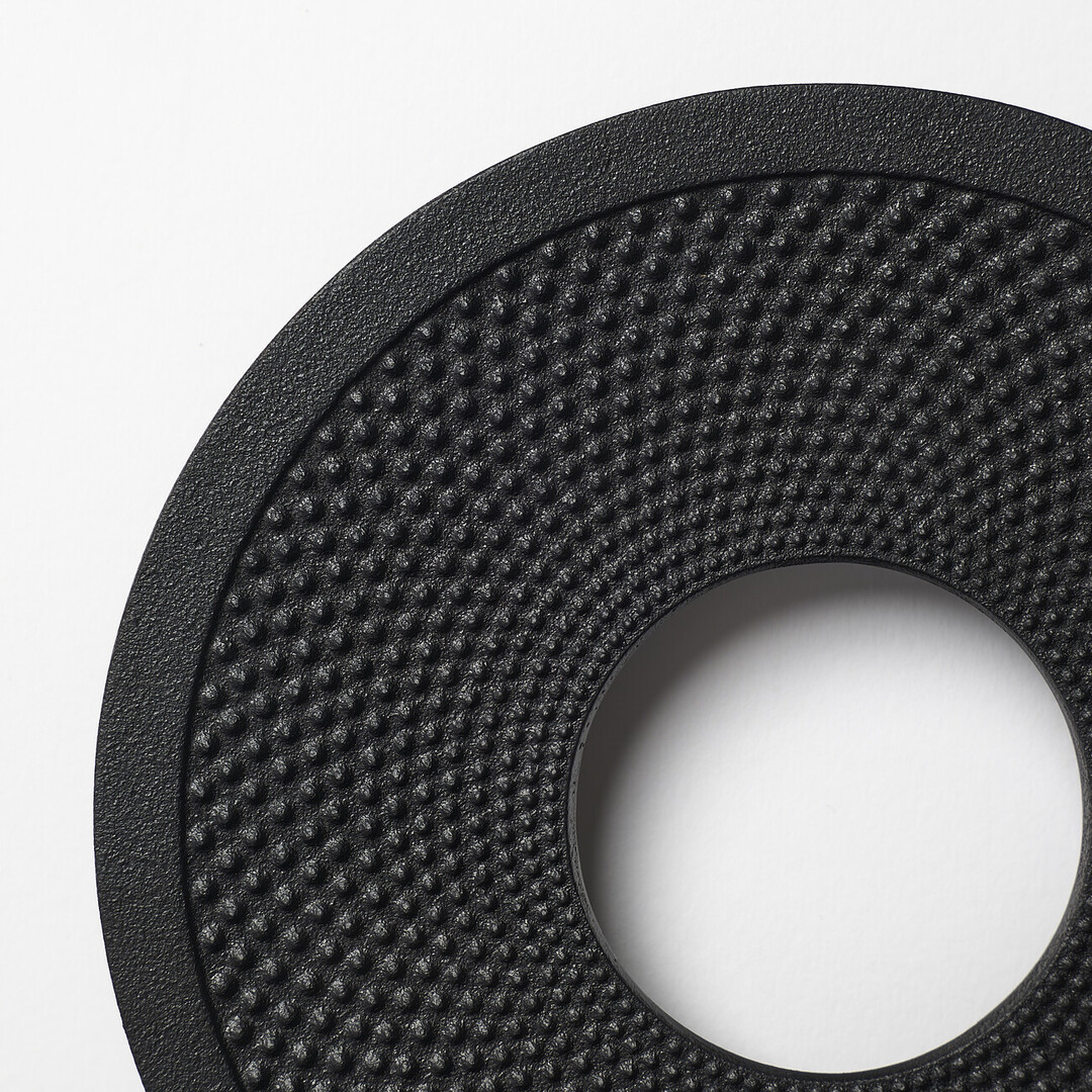 A cast iron black trivet shaped like a donut with a textured surface by OIGEN Foundry Co., Ltd. from Japan House London.