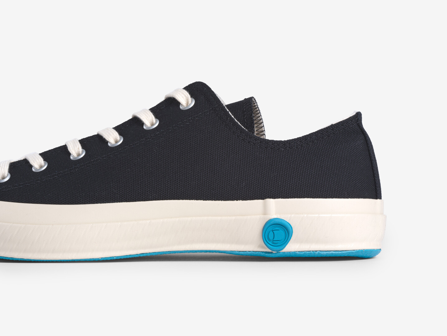 A black canvas shoe with a white sole and blue marking of the brand Shoes like Pottery from Japan House London.