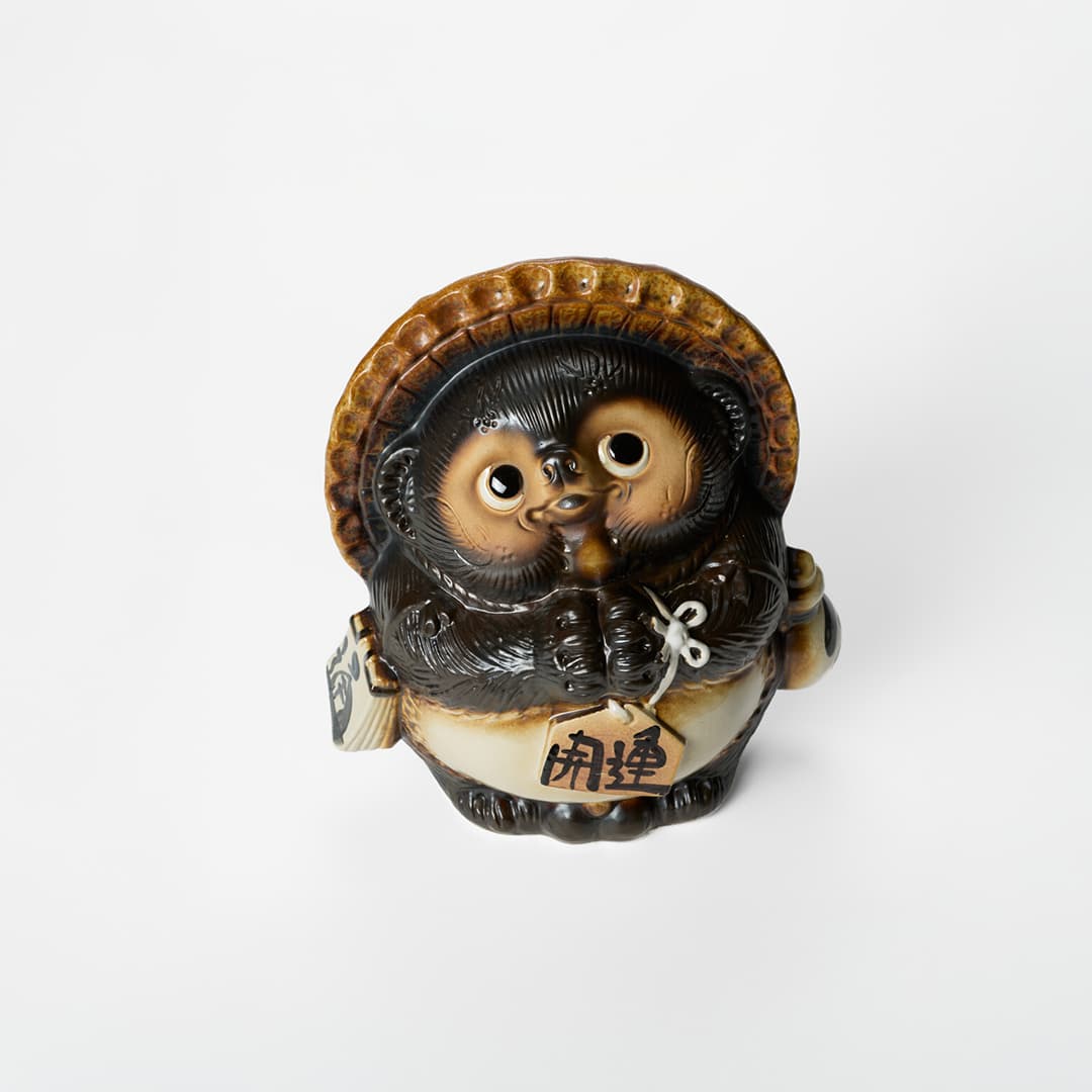 A shigaraki-yaki tanuki statue wearing a hat and holding a bottle of sake from Japan House London