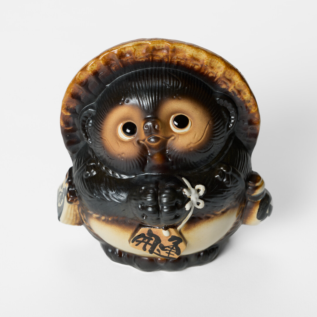 A male Shigaraki-yaki tanuki wearing a straw hat and holding a sake bottle from Japan House London