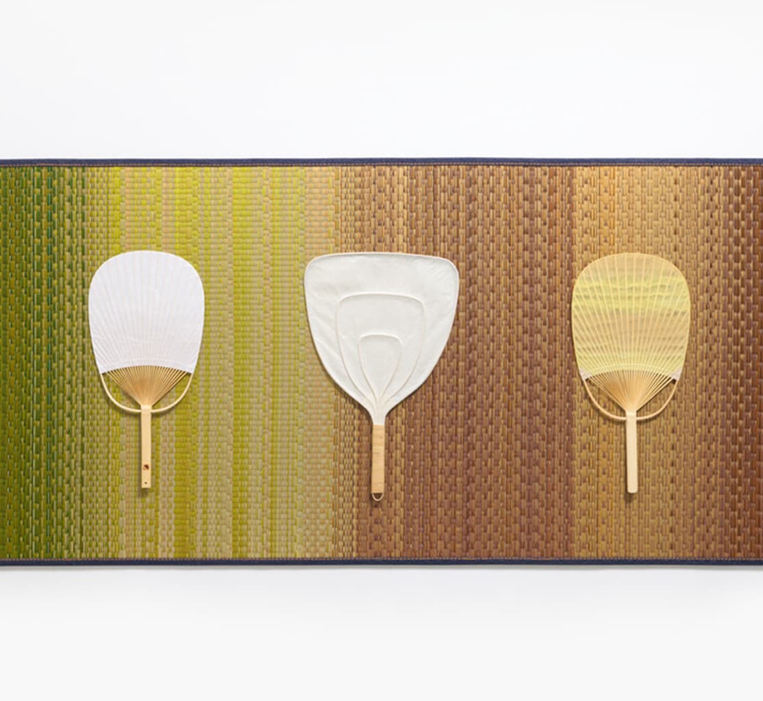 A multicoloured tatami mat with three paper hand fans from Japan House London