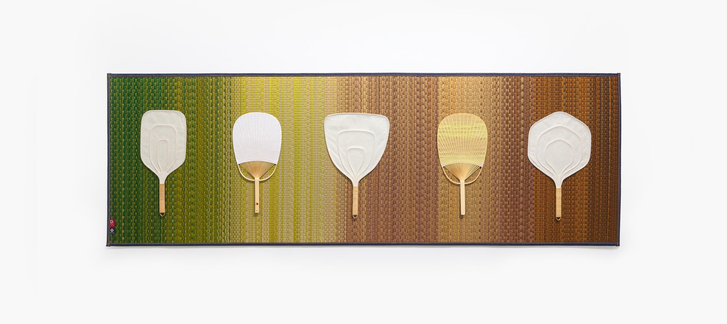 A multicoloured tatami mat with five paper hand fans from Japan House London