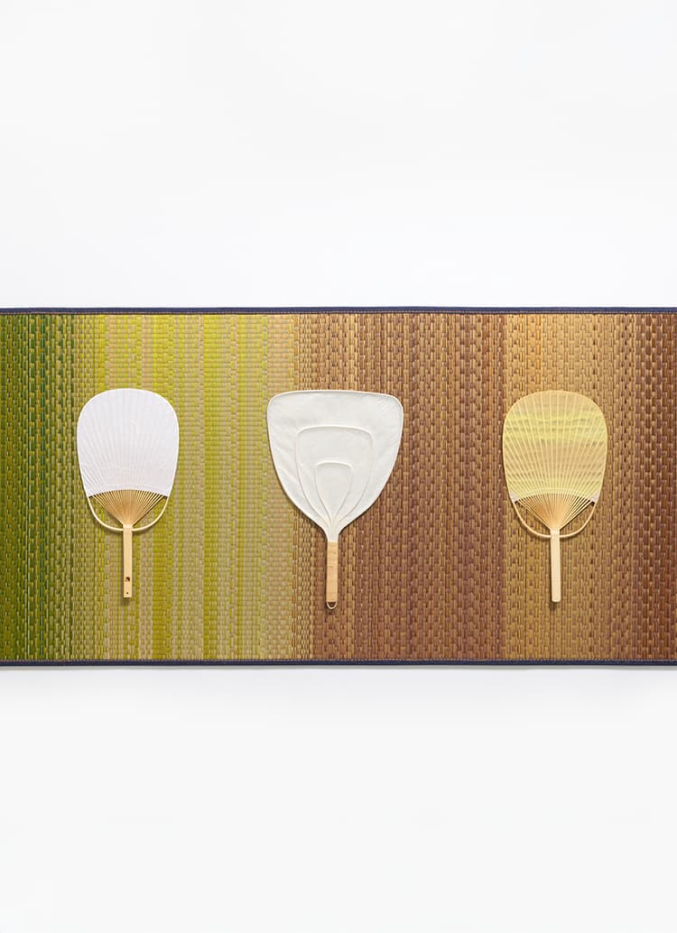 A multicoloured tatami mat with three paper hand fans from Japan House London