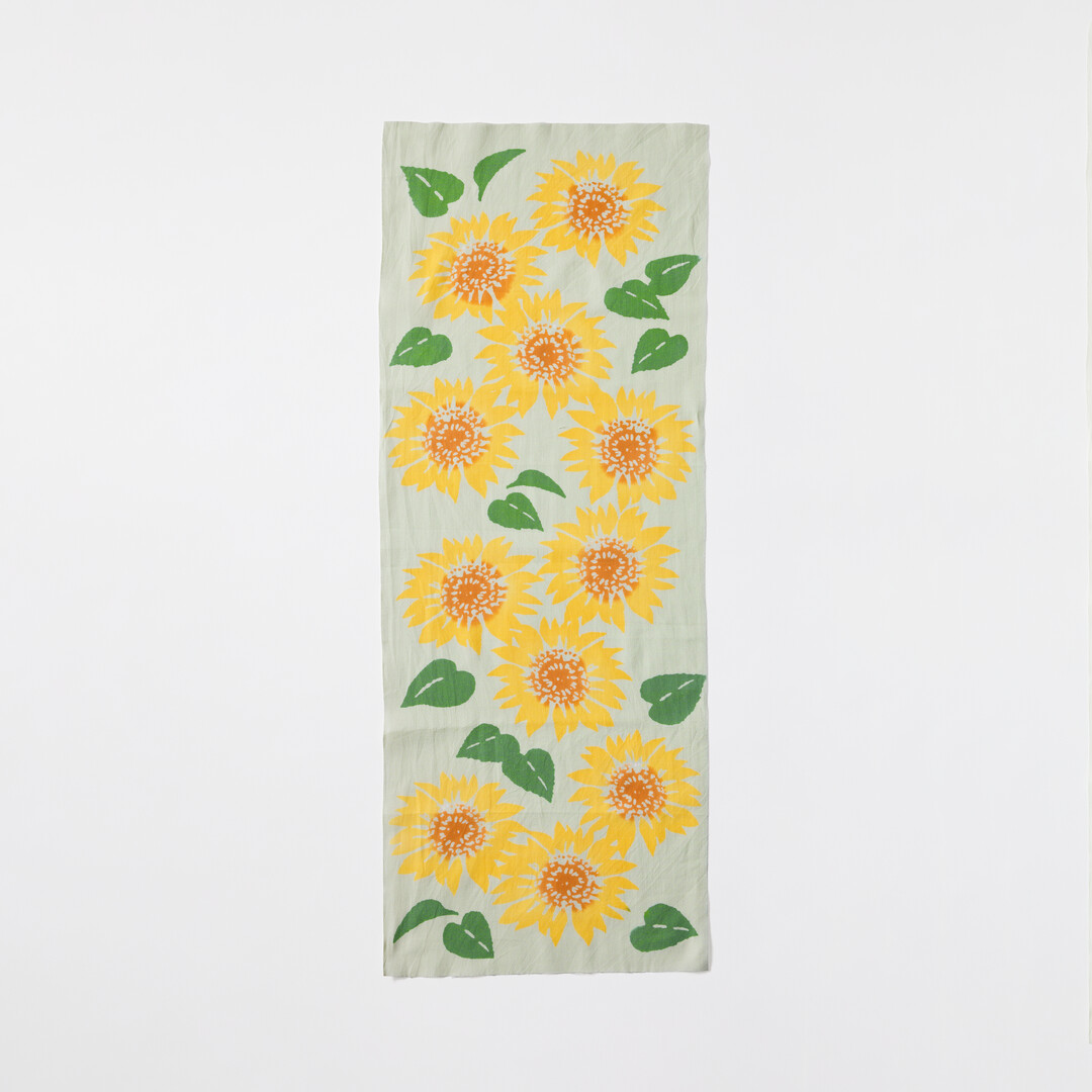 A tenugui with brightly coloured Sunflower on a light blue background by Kamawanu from Japan House London