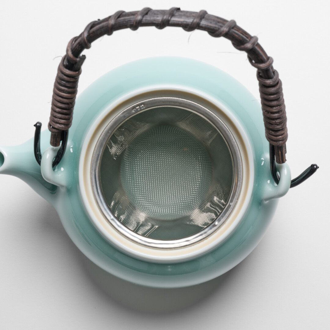 Nabeshima Celadon teapot in turquoise with natural fibre woven handle and tea strainer from Japan House London.