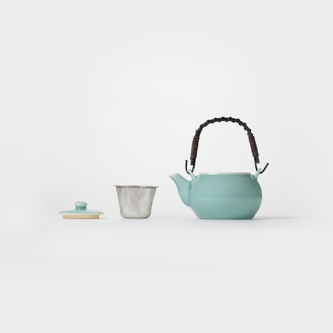 Nabeshima Celadon teapot in turquoise with natural fibre woven handle and tea strainer from Japan House London.