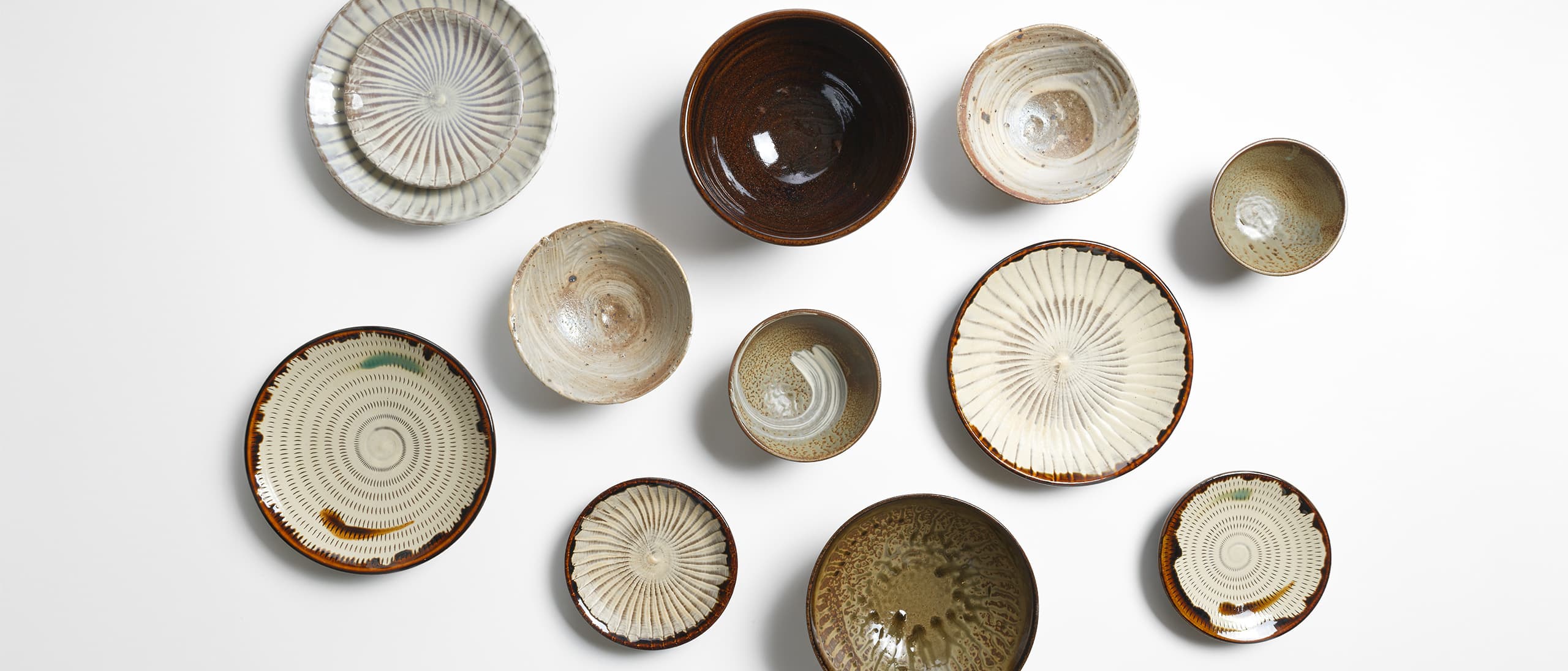 Many Koishiwara Ware and Takatori Ware plates and bowls scattered across the white background from Japan House London.