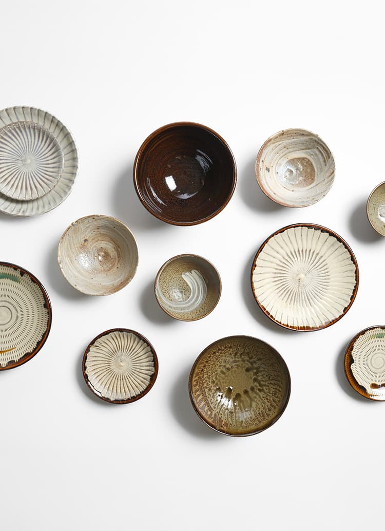 Many Koishiwara Ware and Takatori Ware plates and bowls scattered across the white background from Japan House London.